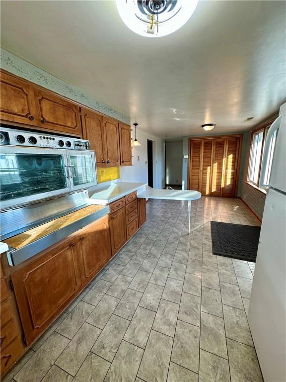 kitchen featuring brown cabinets, light tile patterned floors, freestanding refrigerator, open floor plan, and oven