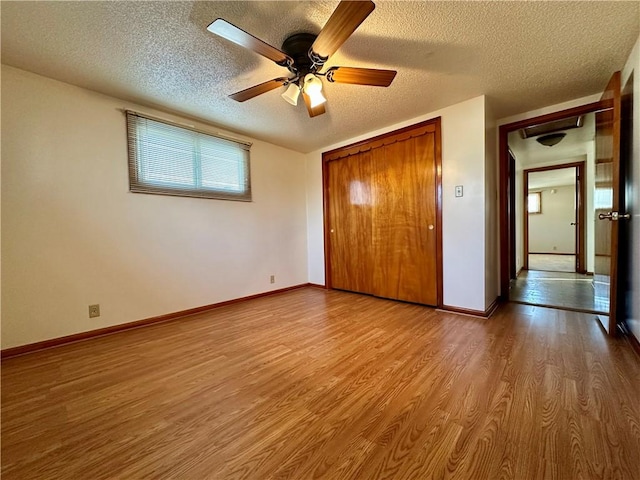 unfurnished bedroom with a textured ceiling, a closet, baseboards, and wood finished floors