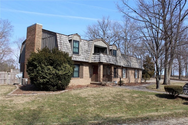 view of front facade with a balcony, brick siding, fence, a gambrel roof, and a front yard