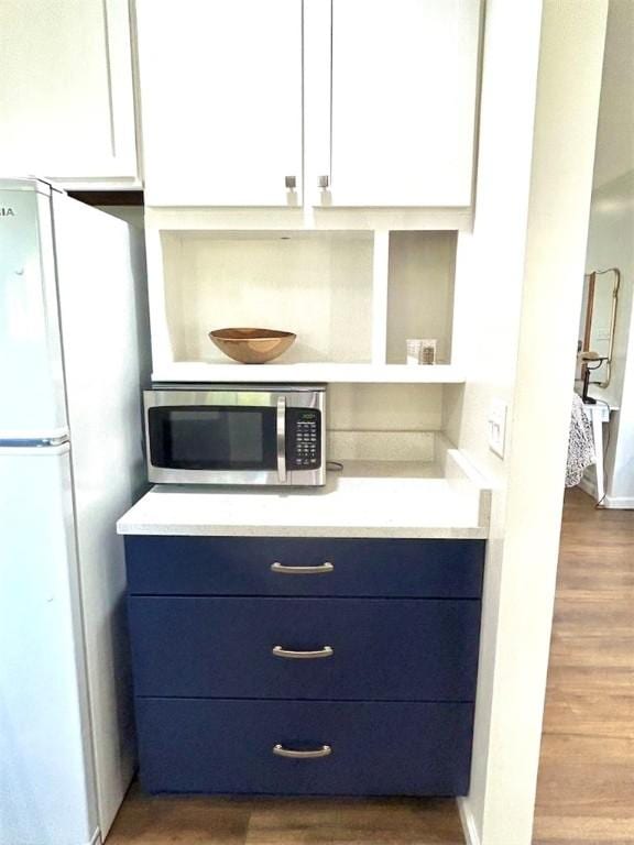 20786 Heritage Ln, Marshall, IL 62441 - kitchen featuring stainless steel microwave, freestanding refrigerator, blue cabinetry, and wood finished floors