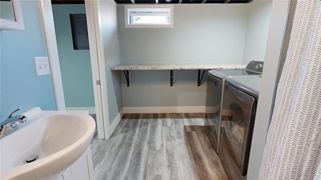 clothes washing area with baseboards, laundry area, separate washer and dryer, a sink, and light wood-type flooring