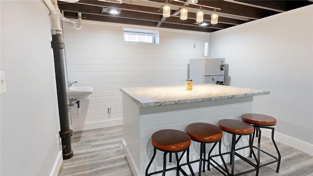 kitchen with light stone counters, light wood-style flooring, a breakfast bar area, and baseboards