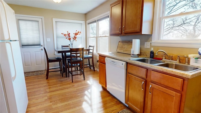 kitchen with light countertops, light wood-type flooring, brown cabinets, white appliances, and a sink