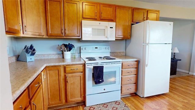 kitchen with light wood-style flooring, brown cabinets, white appliances, and light countertops