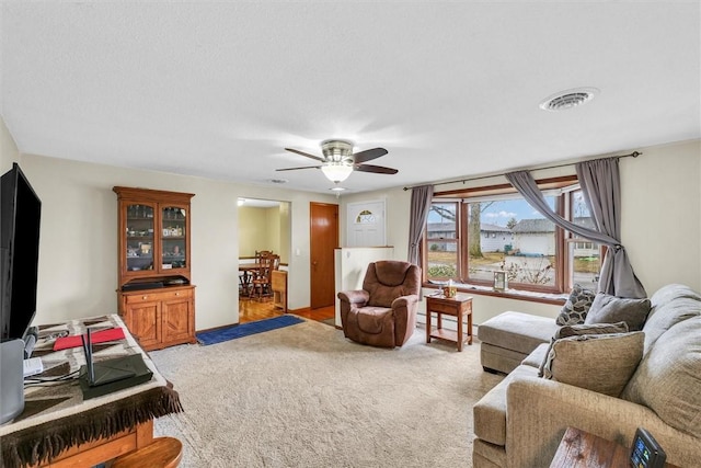 living room with light carpet, visible vents, baseboard heating, and a ceiling fan