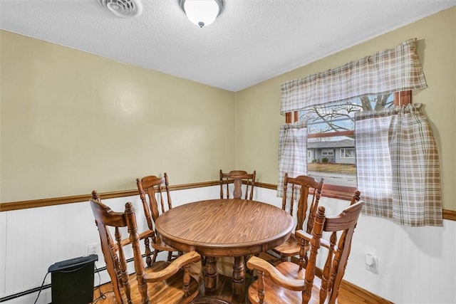 dining space featuring a baseboard radiator, visible vents, a textured ceiling, and wood finished floors