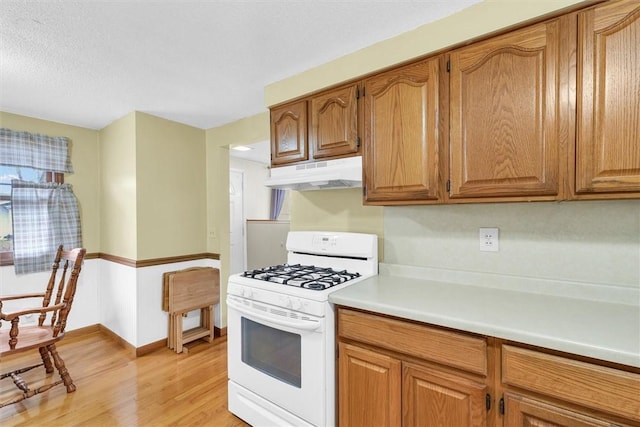 kitchen featuring under cabinet range hood, white range with gas cooktop, light countertops, light wood-type flooring, and brown cabinetry