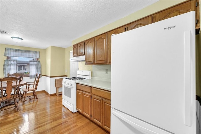 kitchen with under cabinet range hood, white appliances, light countertops, light wood-type flooring, and brown cabinets