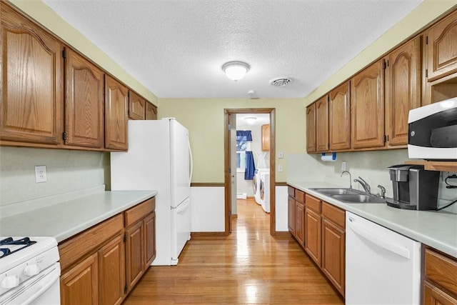 kitchen with white appliances, light wood finished floors, visible vents, washer / clothes dryer, and a sink