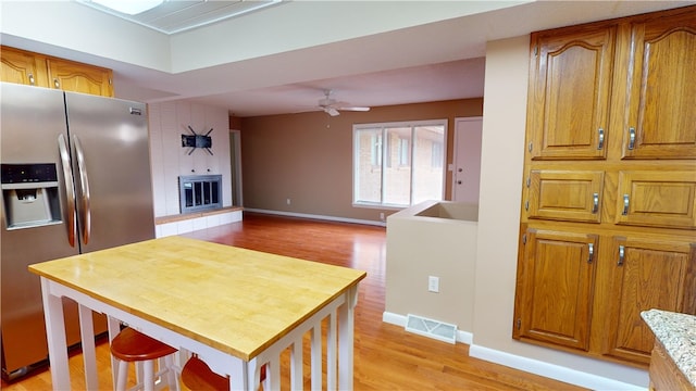 kitchen featuring ceiling fan, a fireplace, stainless steel fridge, and light hardwood / wood-style flooring