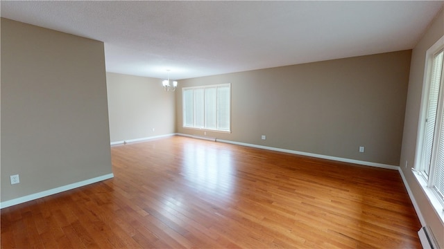 spare room with an inviting chandelier, baseboard heating, and light wood-type flooring