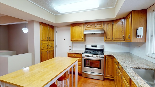 kitchen featuring light stone counters, decorative light fixtures, stainless steel range with gas stovetop, light hardwood / wood-style floors, and backsplash