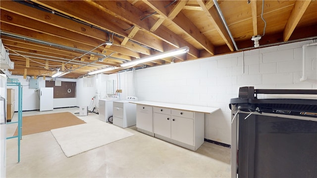 basement featuring washing machine and dryer, white fridge, and electric panel