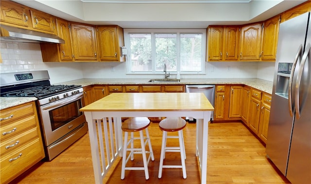 kitchen featuring sink, stainless steel appliances, light hardwood / wood-style floors, and a breakfast bar