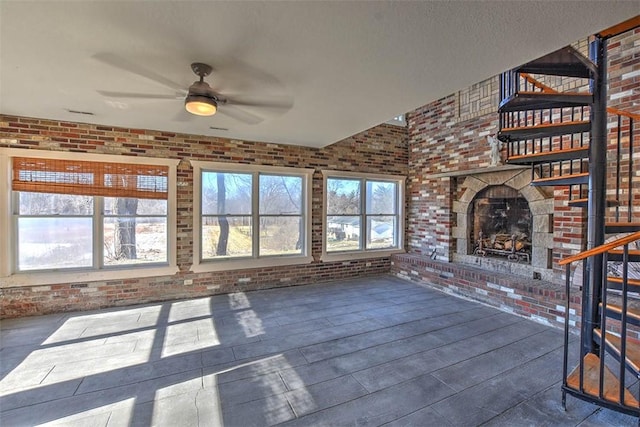 unfurnished living room with ceiling fan, brick wall, and a fireplace