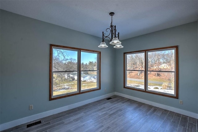 unfurnished dining area featuring dark hardwood / wood-style flooring, a chandelier, and a wealth of natural light