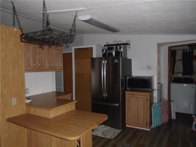 kitchen with brown cabinetry, freestanding refrigerator, dark wood-style floors, washer / clothes dryer, and stainless steel microwave