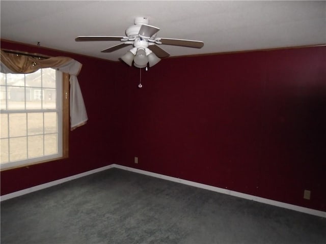 empty room with a ceiling fan, dark colored carpet, and baseboards