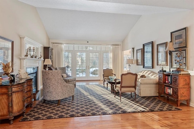 sitting room with french doors, hardwood / wood-style floors, high vaulted ceiling, and a premium fireplace