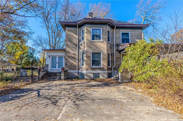 rear view of house with fence, french doors, brick siding, and a chimney