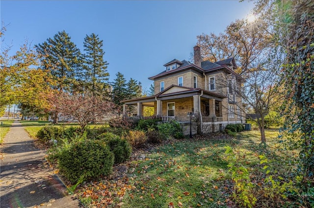 view of front of house with stone siding, covered porch, a chimney, and a front yard