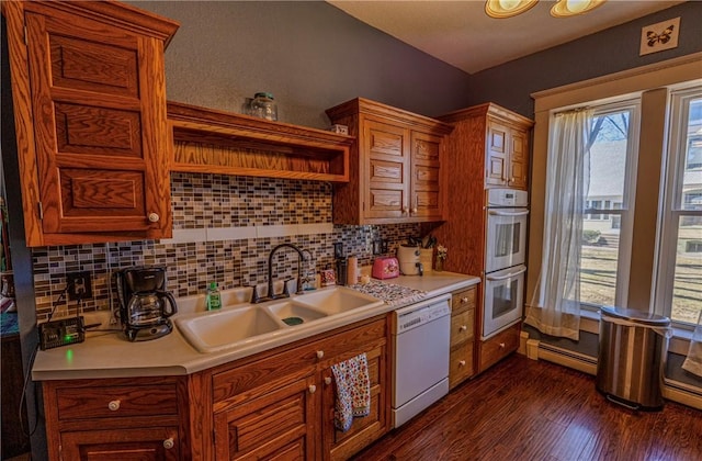 kitchen with a sink, double oven, white dishwasher, light countertops, and baseboard heating