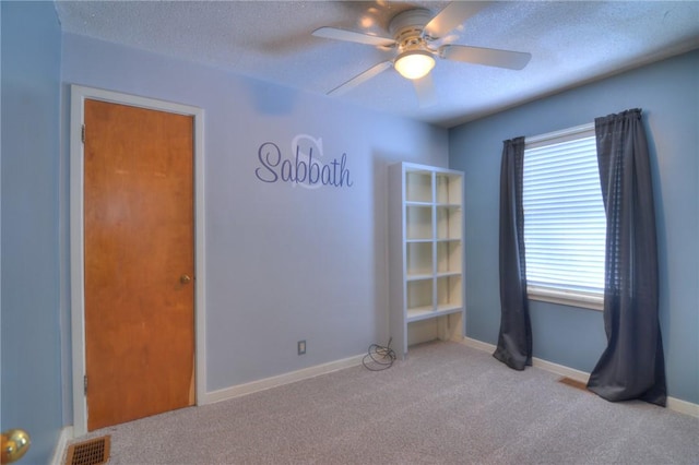 empty room with ceiling fan, light colored carpet, and a textured ceiling