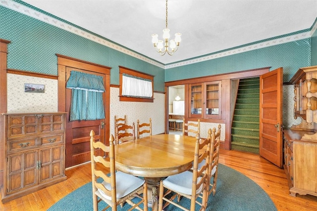 dining area with light wood-type flooring, wallpapered walls, stairs, and a chandelier