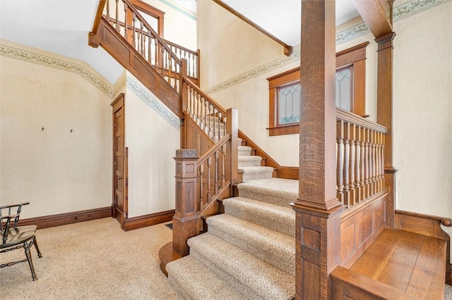 staircase with decorative columns, a high ceiling, baseboards, and carpet flooring