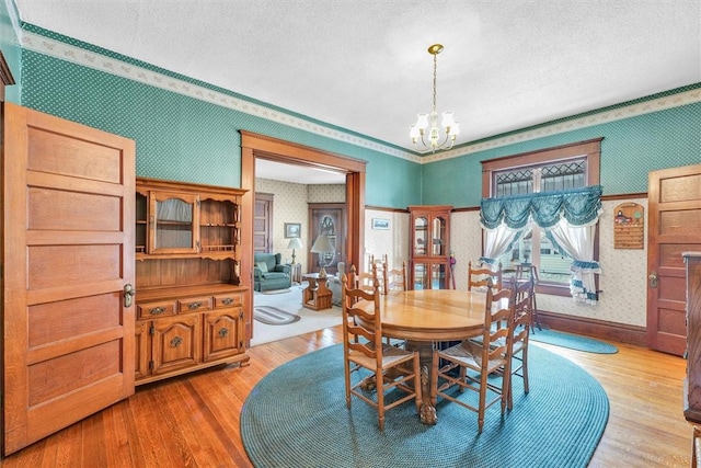 dining room featuring wallpapered walls, a notable chandelier, light wood finished floors, and a textured ceiling