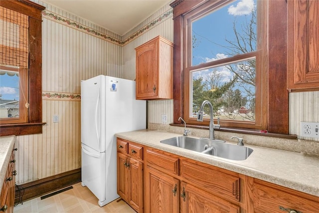 kitchen with light countertops, visible vents, freestanding refrigerator, a sink, and wallpapered walls