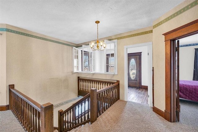 hallway featuring wallpapered walls, carpet, a textured ceiling, an upstairs landing, and a chandelier