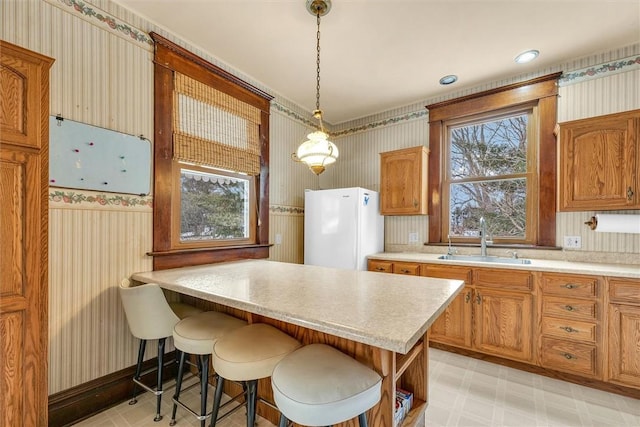 kitchen featuring wallpapered walls, freestanding refrigerator, light countertops, light floors, and a sink