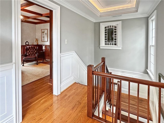 corridor with an upstairs landing, a decorative wall, crown molding, light wood finished floors, and a wainscoted wall