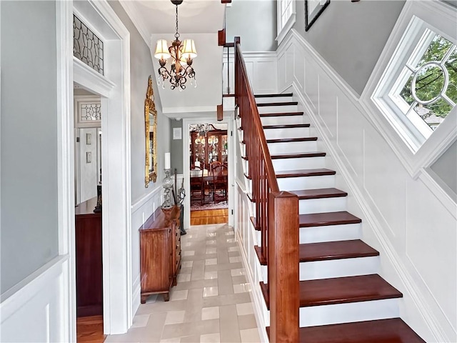 stairway with a chandelier, a decorative wall, a wainscoted wall, and tile patterned floors