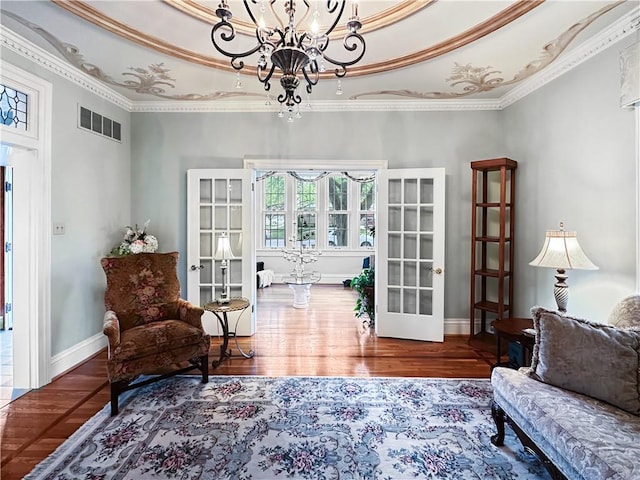 living area featuring a chandelier, french doors, ornamental molding, a tray ceiling, and wood finished floors