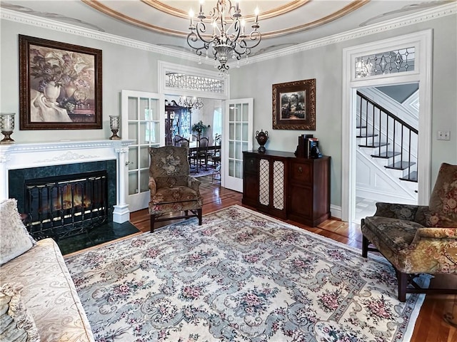 living area featuring a chandelier, wood finished floors, stairs, a raised ceiling, and ornamental molding