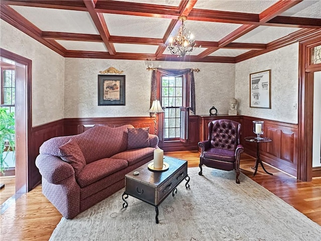 living area with wood finished floors, coffered ceiling, beamed ceiling, a chandelier, and wainscoting