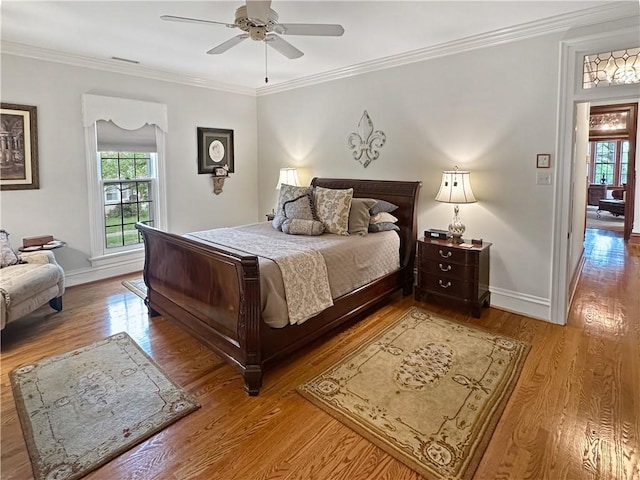 bedroom featuring multiple windows, wood finished floors, baseboards, ornamental molding, and a ceiling fan