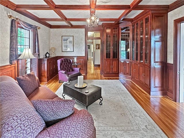 living area featuring light wood-style floors, coffered ceiling, a wainscoted wall, a chandelier, and beamed ceiling