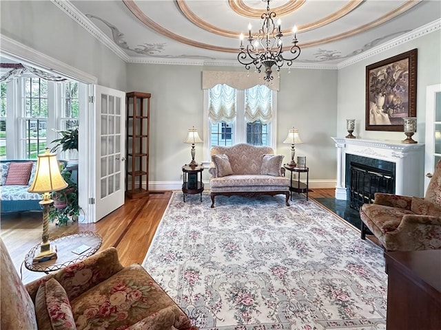 living area with a tray ceiling, plenty of natural light, a chandelier, wood finished floors, and ornamental molding