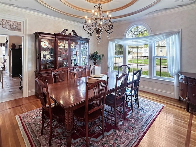 dining space featuring a chandelier, light wood-type flooring, ornamental molding, and a tray ceiling