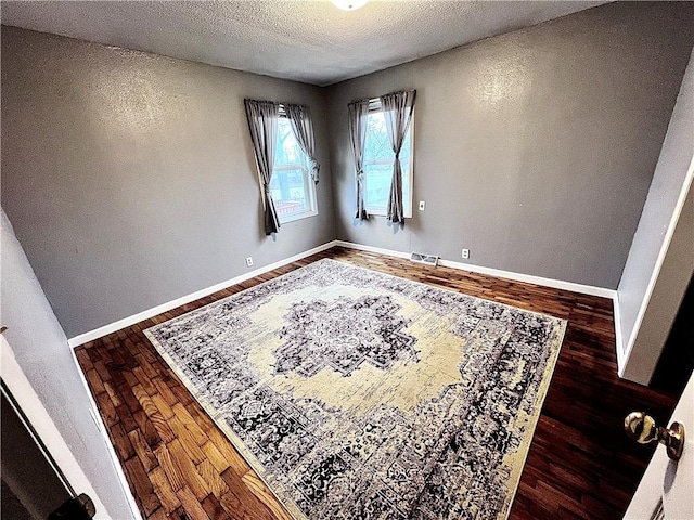 unfurnished room with a textured ceiling and dark hardwood / wood-style floors