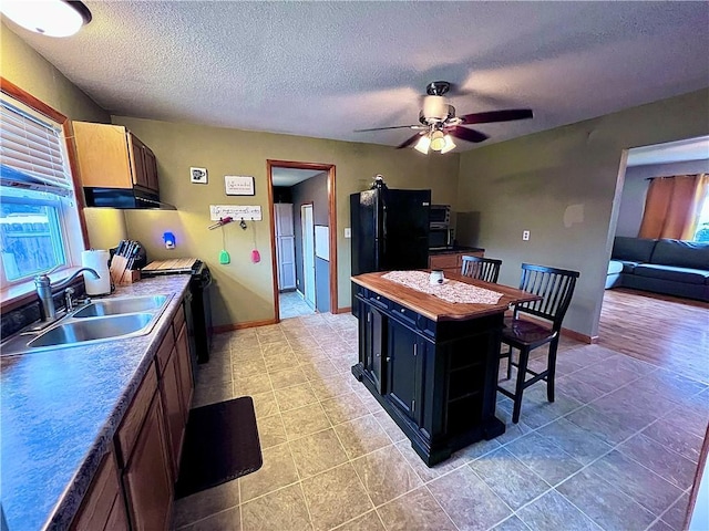 kitchen with black refrigerator, a kitchen breakfast bar, a textured ceiling, and sink