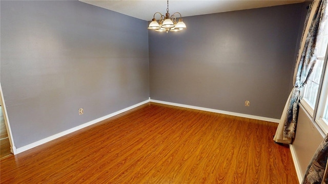 spare room featuring an inviting chandelier, baseboards, and wood finished floors