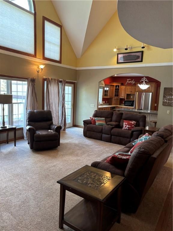 carpeted living room with high vaulted ceiling, plenty of natural light, and arched walkways