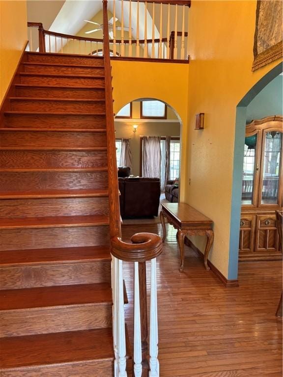 staircase with arched walkways, baseboards, wood finished floors, and a towering ceiling