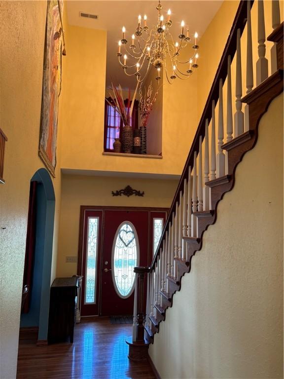 entrance foyer featuring visible vents, a towering ceiling, arched walkways, wood finished floors, and stairway