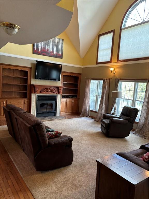 living area with carpet floors, high vaulted ceiling, and a glass covered fireplace