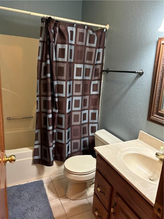 bathroom with tile patterned flooring, vanity, toilet, a textured wall, and shower / bathtub combination with curtain